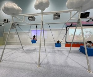 Girls on indoor swings in front of projector screens.